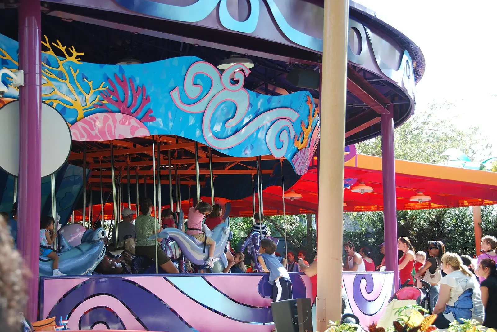 Children riding sea-creature figures on a colourful ocean-themed carousel at SeaWorld Orlando, with parents waiting alongside